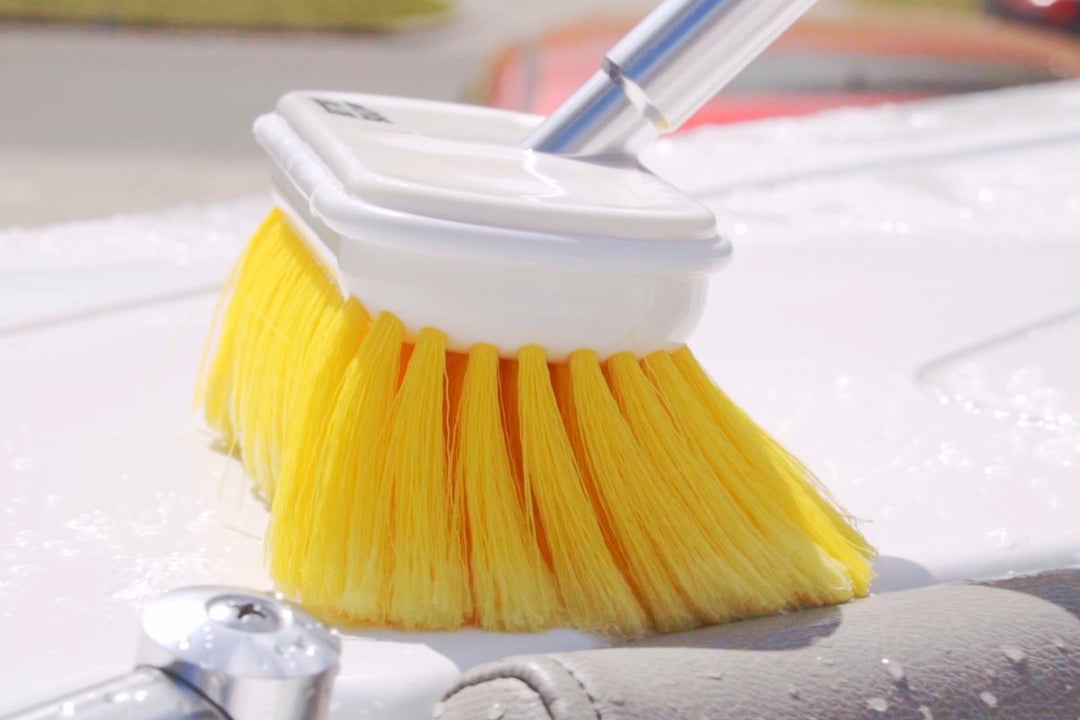 Soft deck brush on an extension rod scrubbing a soapy boat deck